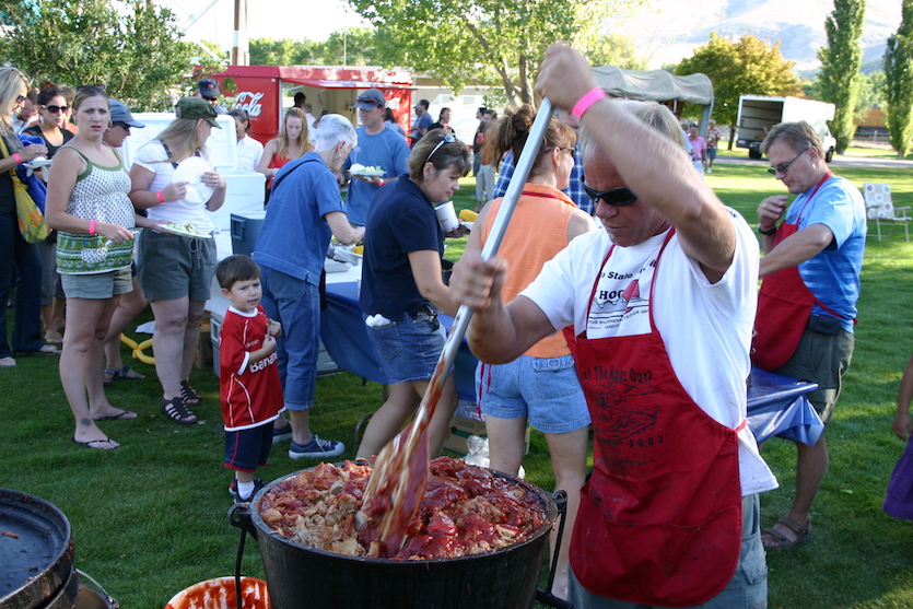 Photo from scene of a previous Pig Out; person mixing bbq with people in background