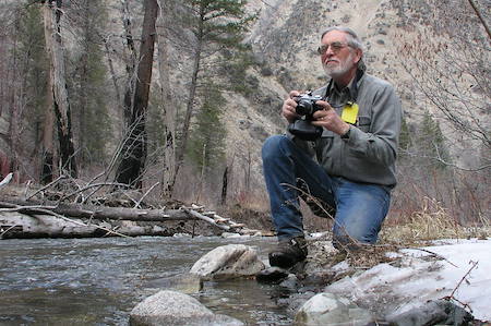Minshall kneeling on a rock by a stream with a camera in hand.