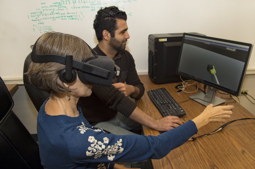 Photo of researcher with virtual reality headset on with student working computer in the background.