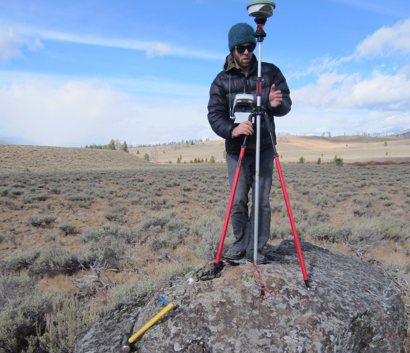 Chris Tennant in the field standing on a rock setting up a measuring instrument on a tripod.