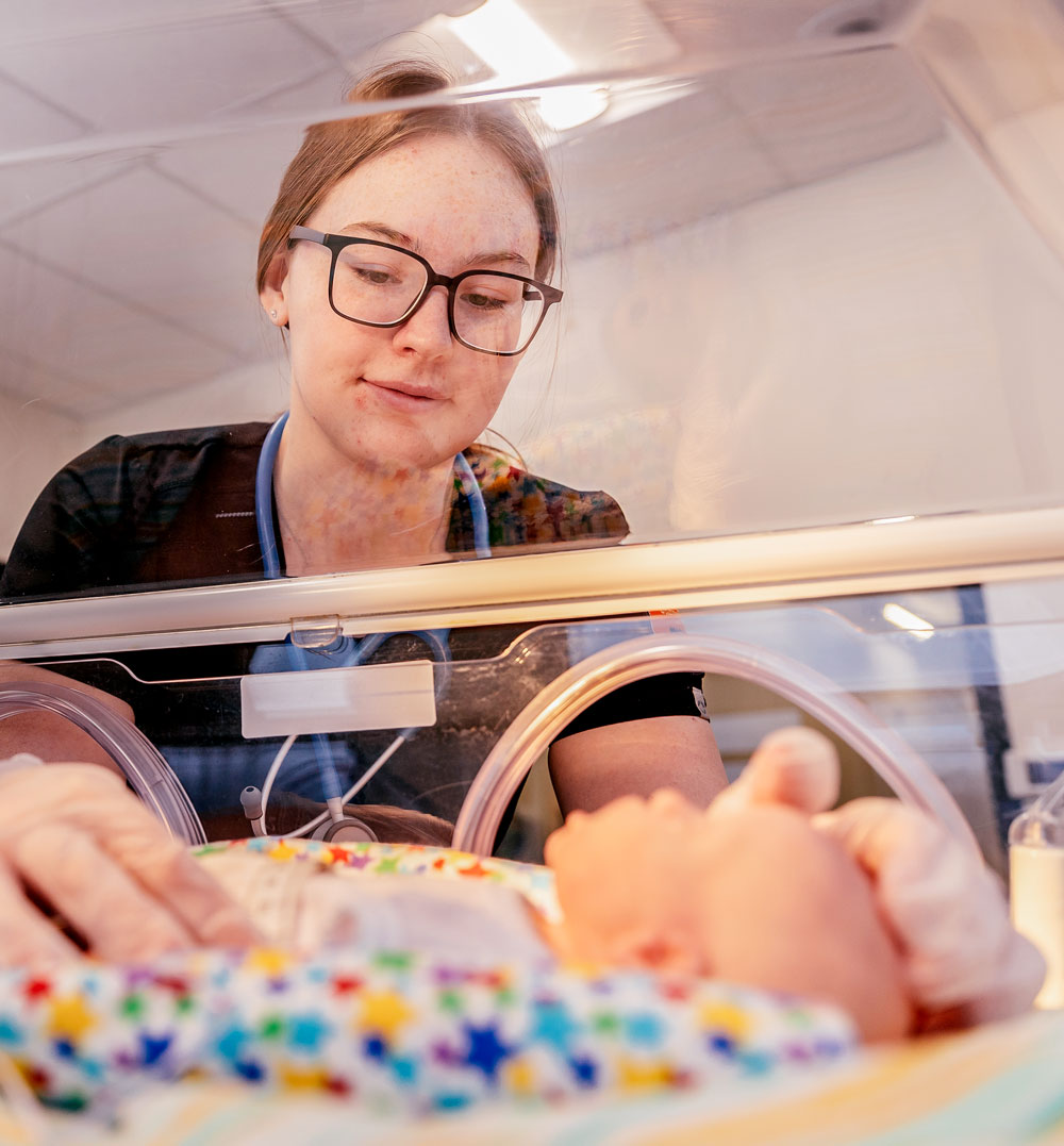 A nursing student practices caring for a baby using a simulated incubator.